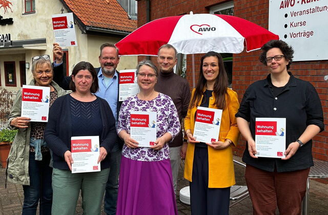 Gruppenbild: 7 Menschen stehen draußen, lächeln und halten DIN A4 große Broschüren in die Kamera.