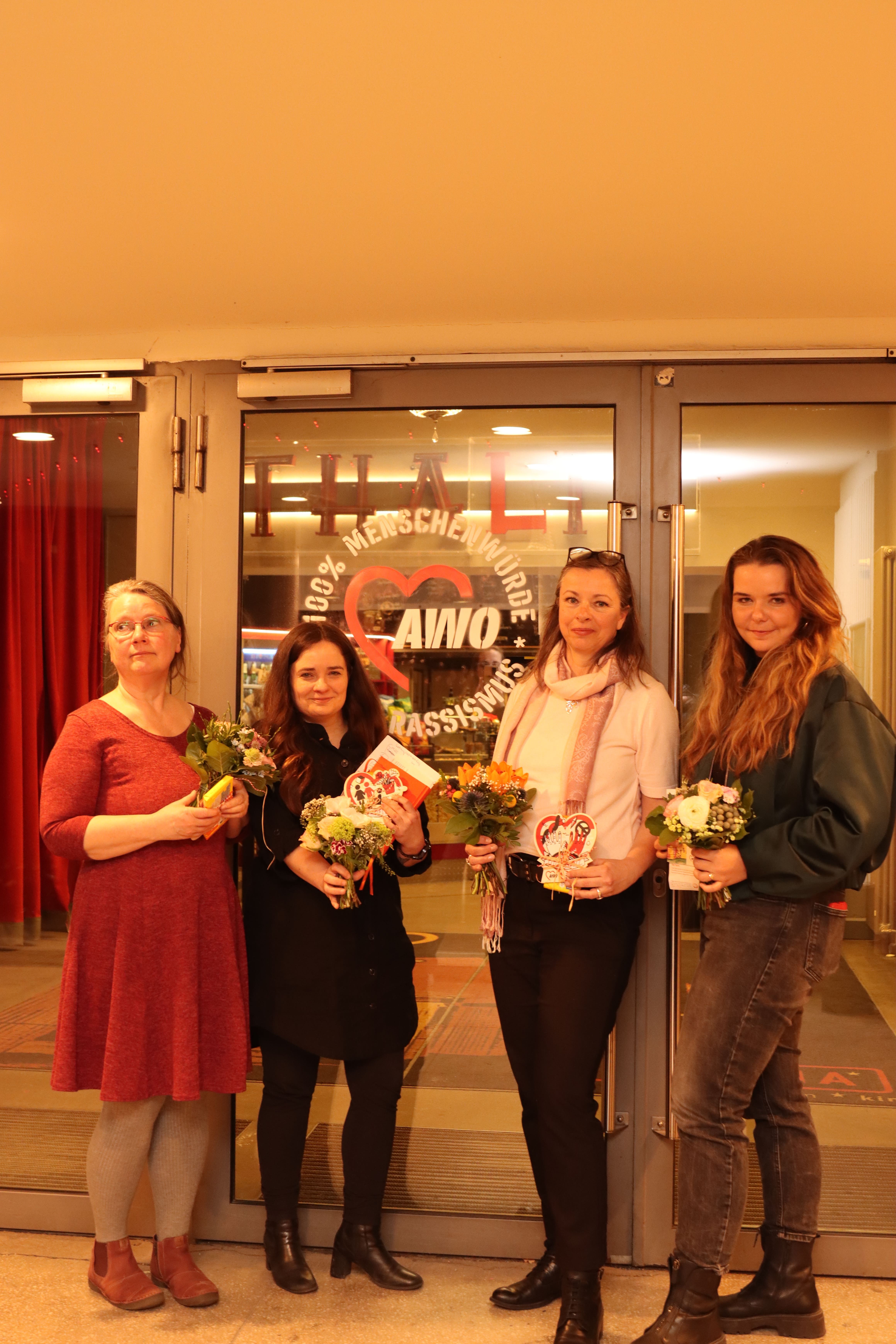 Gruppenbild. 4 Frauen im Foyer des Thalia Kino vor Glastüren. Alle haben kleine Blumensträuße und kleine Geschenke in der Hand.