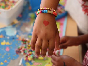 Kind hält Hand mit Perlenarmband und einem kleinen ruten Herz in die Kamera.
