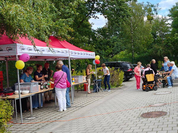 Hof. Links Getränke und Bratwurststand. Rechts Menschen an Tischen beim Essen.