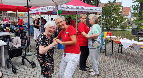Zwei Helferinnen in roten AWO T-Shirts tanzen fröhlich mit zwei alten Damen. Die Tanzenden im Vordergrund lächeln in die Kamera.