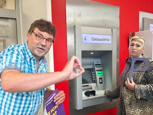 Eine Frau steht an einem Geldautomaten und hält ein großes P vor sich.