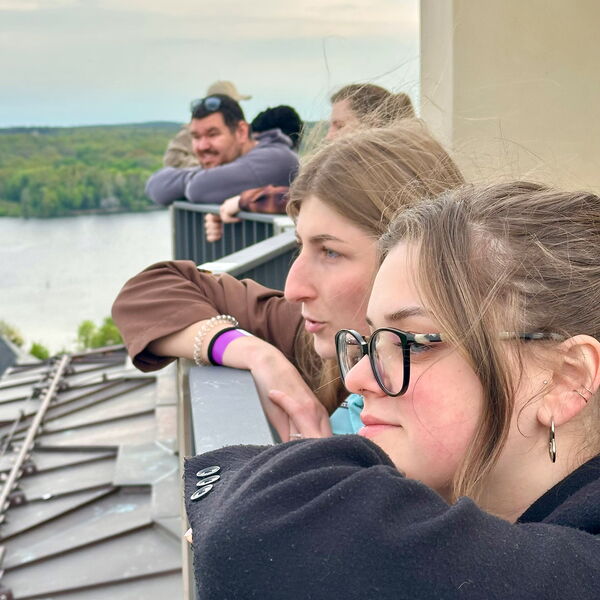 Menschen lehnen sich gegen das hohe Geländer einer Aussichtsplattform und genießen die Aussicht.