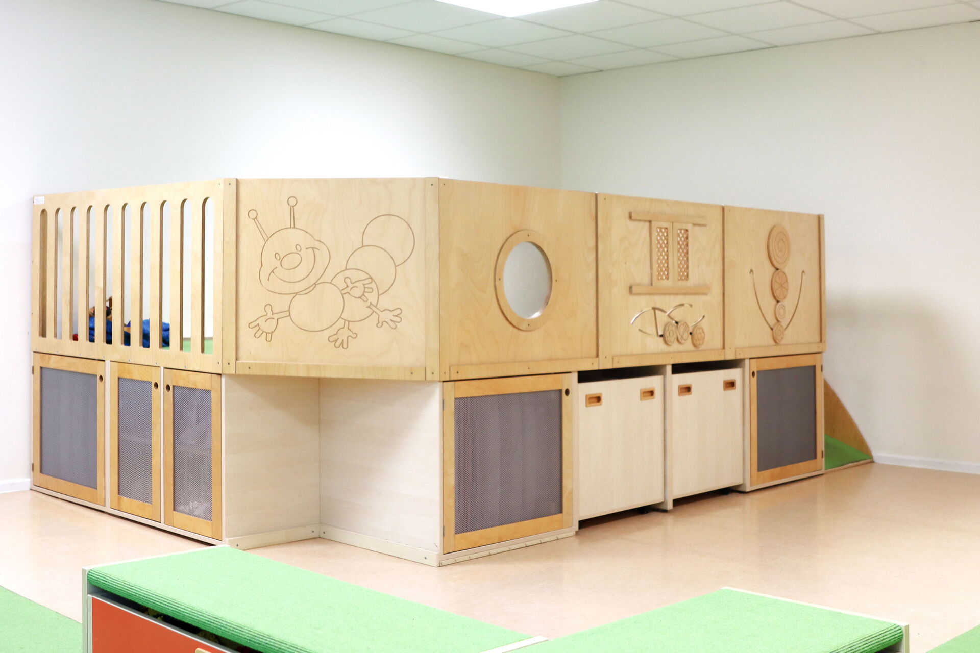 Holz gefertigte Spiel- und Kletterlandschaft für Kinder. Verschiedenen Elementen: einer erhöhten Spielfläche mit Geländer, unterschiedlichen Staufächern, einer kleinen Rutsche und an der Wand.