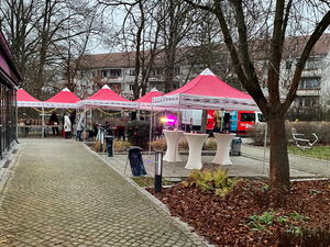 5 rote AWO Pavillons geschmückt mit Lichterketten aus der Ferne. Unter einem Pavillion stehen drei weiße Stehtische.