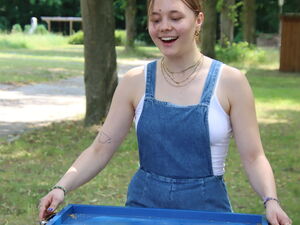 Eine Frau in Latzhose die lachend versucht Bälle in Ausbuchtungen eines beweglichen Bretts zu befördern.