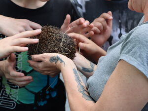 Frau hält Igel in beiden Händen um sie rum neugierige Schüler, die die Stacheln des Igels berühren.