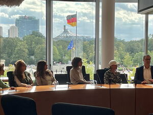 Im Bundestag, 5 Frauen, ein Mann an einem Tisch für großer Fensterfront. Draußen weht im Hintergrund die Deutschland Fahne.