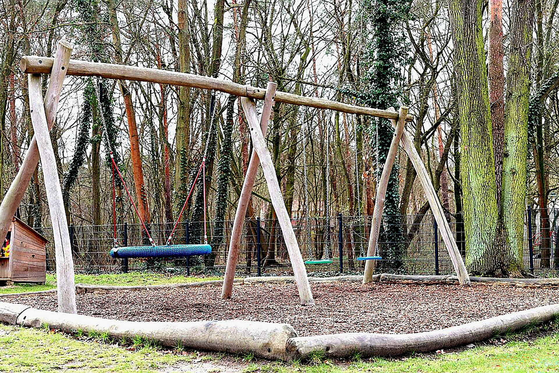 Spielplatz: Schaukeln. Dahinter Bäume.