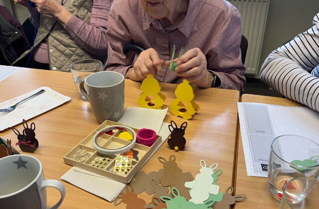 Es wird für Ostern gebastelt. Auf dem Tisch Osterhasen Vorlagen zum falten. Eine alte Frau beim basteln.