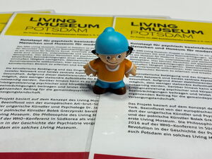 3 laminierte Info-Blätter des Living Museums. In der Mitte darauf steht eine kleine Mainzellmännchen-Figur