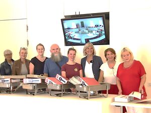 Im Landtag Brandenburg. Langer Tisch hinter dem 10 Personen stehen, darunter ein Mann mit Rauschebart. Vor ihnen stehen Warmhaltebehälter für Essen in denen aber die roten Aktenordner liegen.