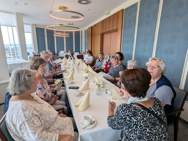 Menschen an Kaffeetafel, fröhlich in Gespräche vertieft. Großer schöner heller Raum.