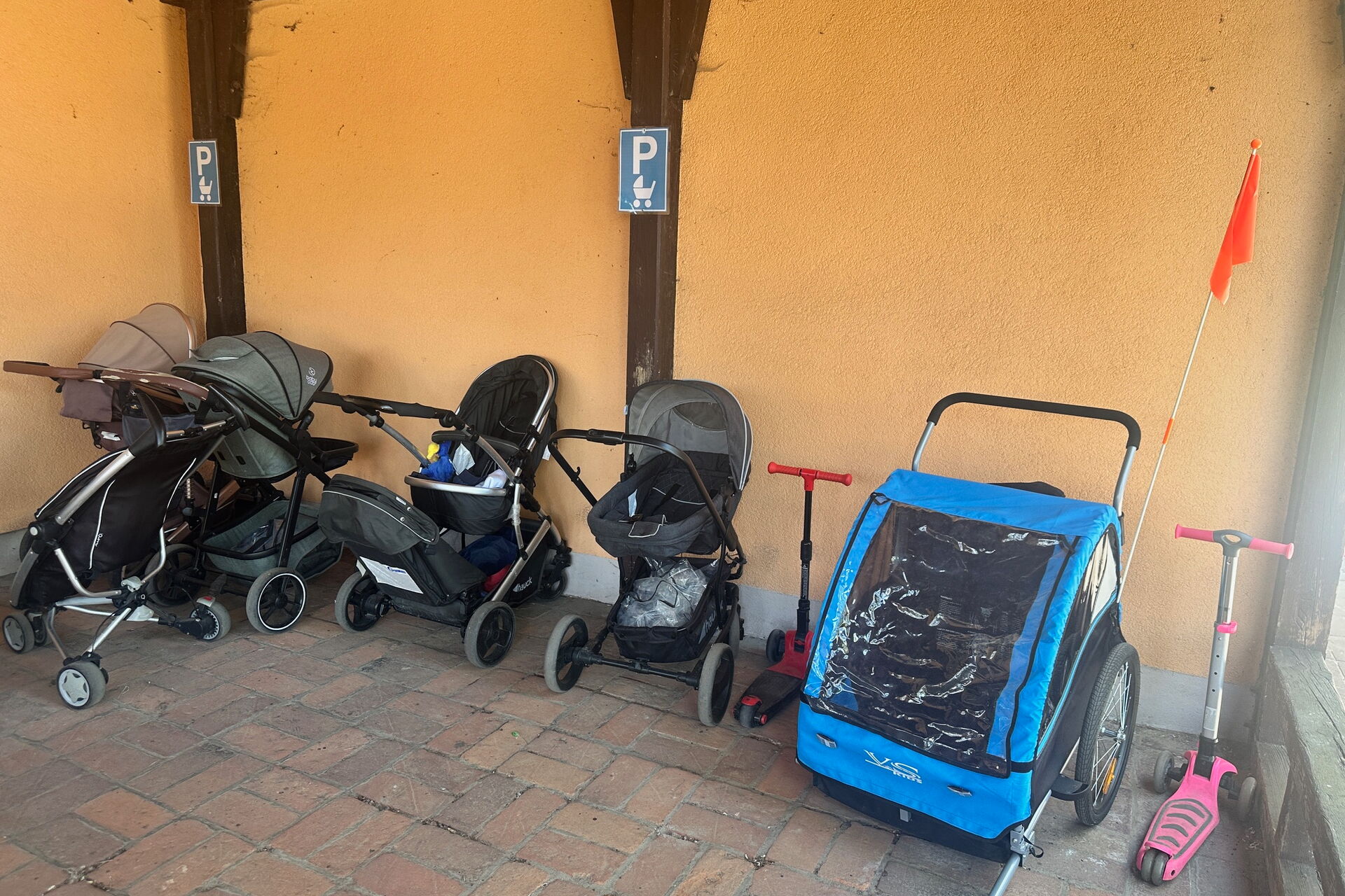 Kinderwagen Parkplatz mit Schild dafür gekennzeichnet. 5 Kinderwägen, ein Kinderfahrradanhänger und 2 Kinderroller parken dort.