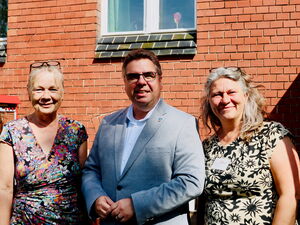 Portrait vor Backsteinwand: 2 Frauen in der Mitte einen Mann.