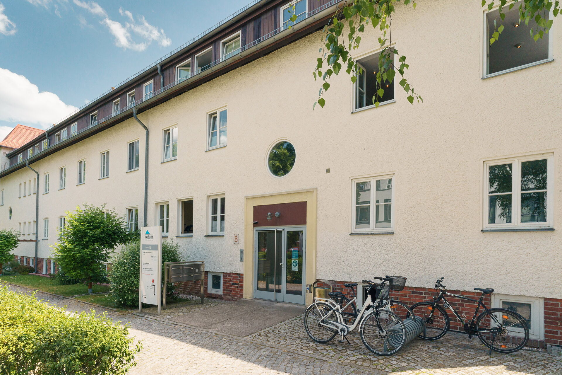 Eingangsbereich eines Hauses mit heller Fassade. Rechts neben dem Eingang ein Fahrradständer.