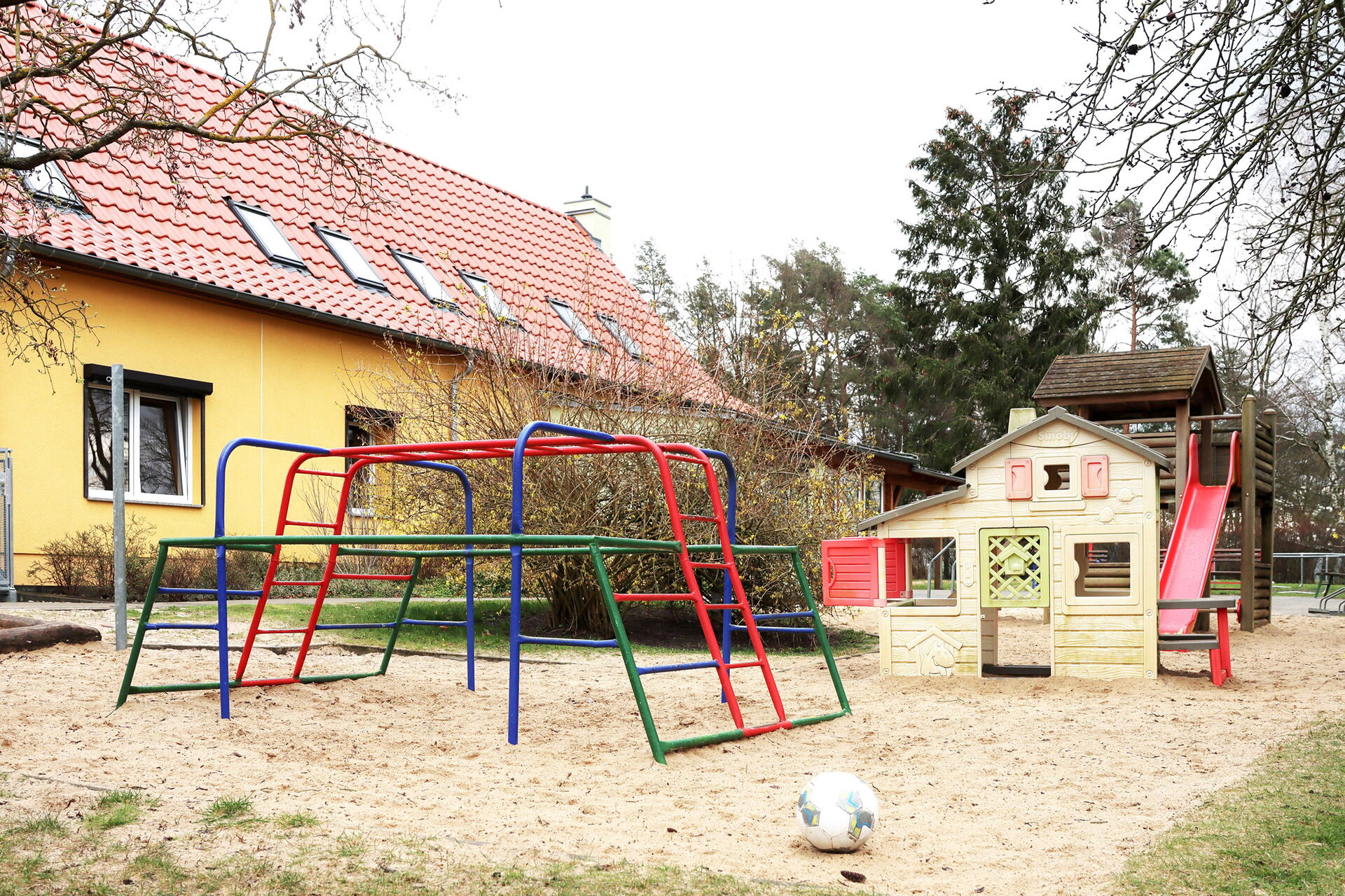 Spielplatz vor einer Kita mit verschiedenen Klettergerüsten und einem Spielhaus.