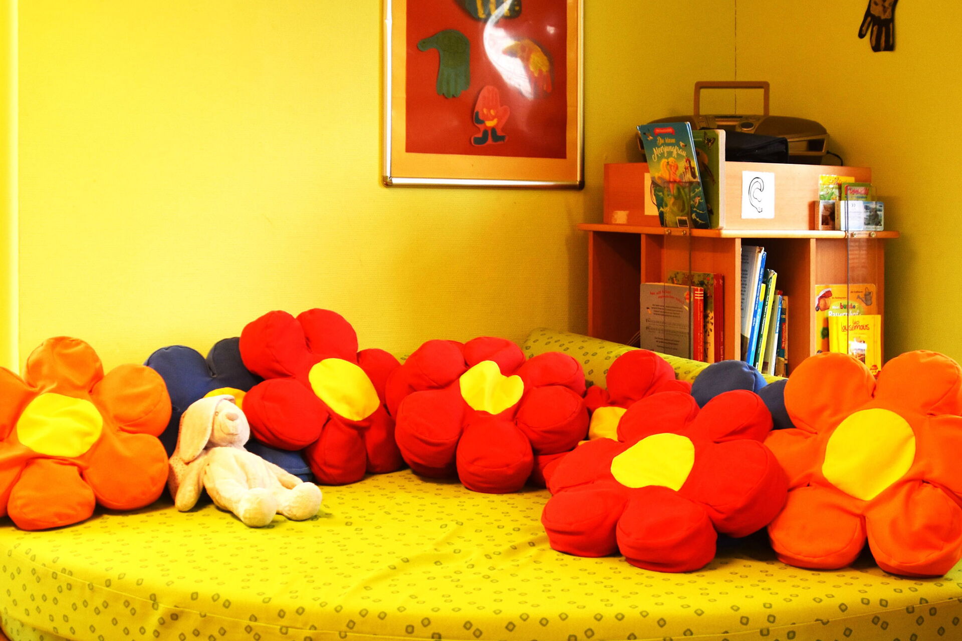 Spielzimmer, großes gelbes Sofa mit großes Kissen in Blumen-Blüten-Form. Gelbe Wände hat der Raum.