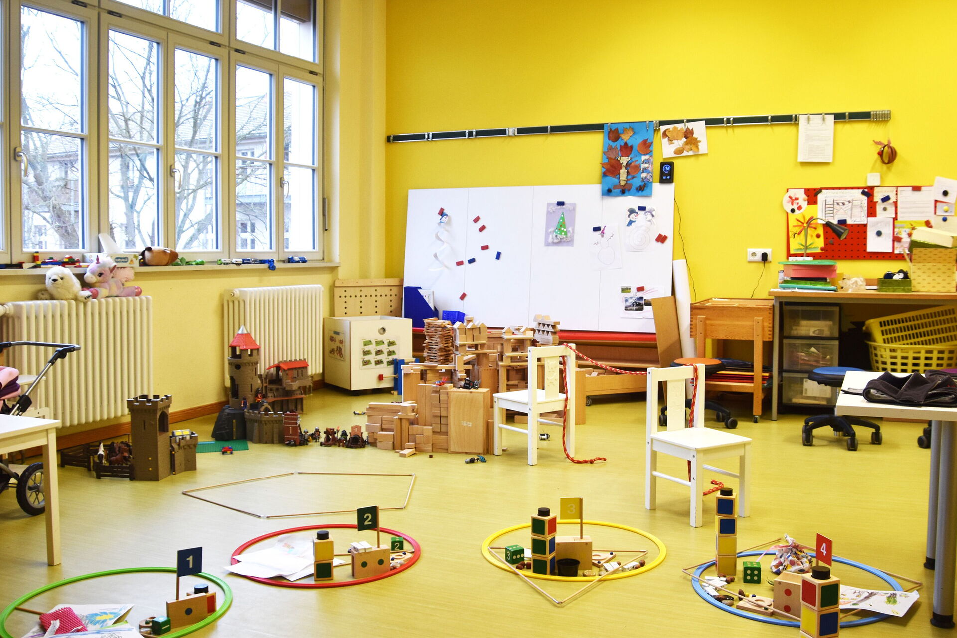 Burgen und Festungen stehen auf dem Fußboden aber auch andere Spielsachen liegen rum. Auf einer Heizung am Fenster sind zwei Kuscheltiere.