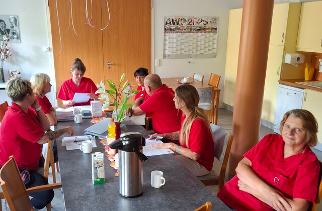 Team in roten AWO Shirts sitzt an einem Tisch mit Unterlagen und Kaffee. Team Sitzung.