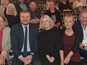 Gruppenbild in Zuschauersaal. 5 Menschen sitzen nebeneinander und lächeln in die Kamera.