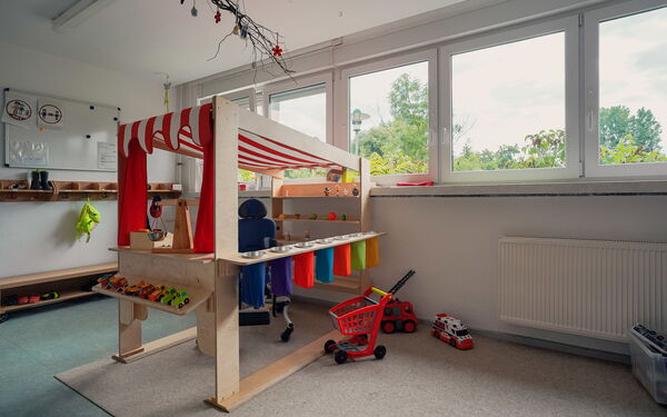 Helles Spielzimmer, mit Kinder Spielzeug, Krankenwagen, Feuerwehr und ein Einkaufsladen für Kinder aus Holz mit rot-weiß gestreifter Markise.