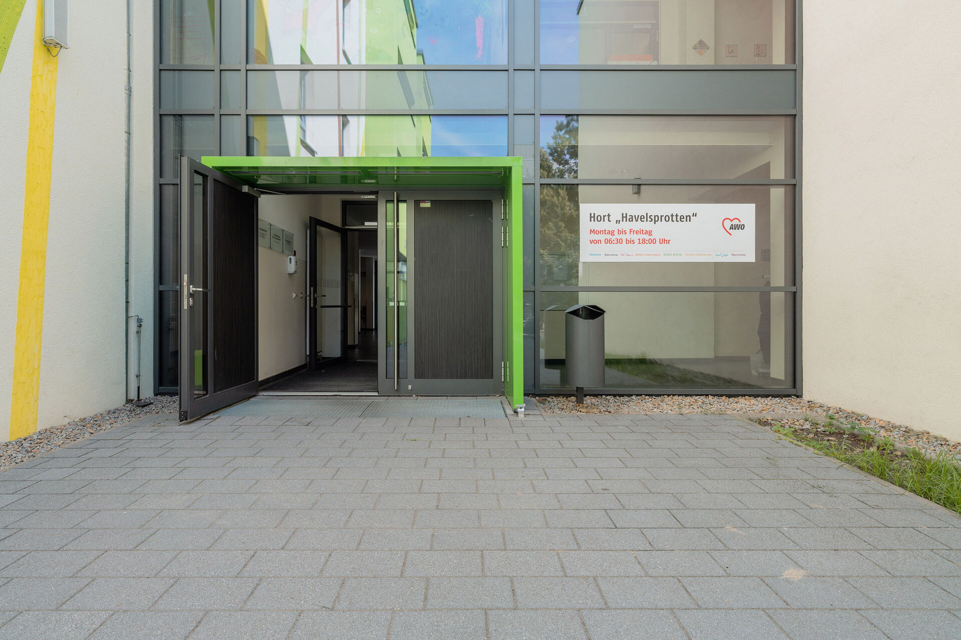 Eingang. Verglast. Große Türen. An der Scheibe rechts ein großes Schild: Hort Havelsprotten.