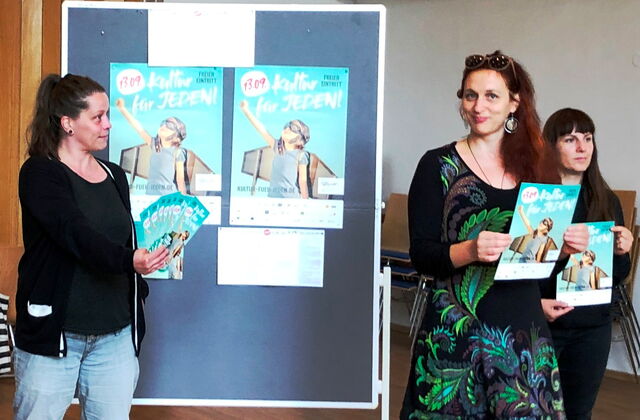 Fünf Personen mit Kultur für Jeden Flyer und Plakaten in den Händen. Dahinter ein Pinntafel an der zwei Plakate angepinnt sind.