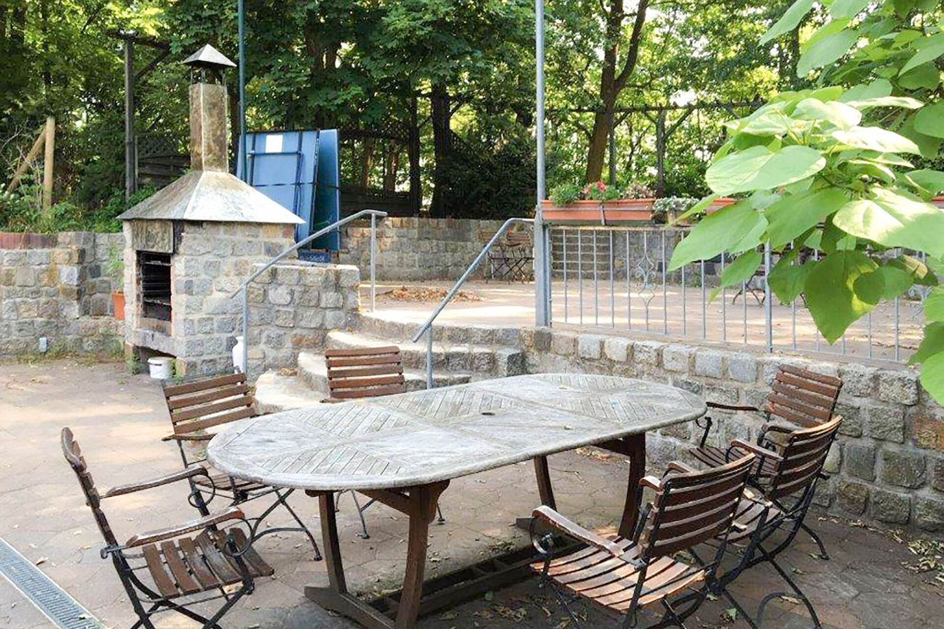 Draußen. Terrasse. Langer Holztisch mit 6 Stühlen. Weiter hinten kleiner Pizze / Brot Backofen aus Stein.