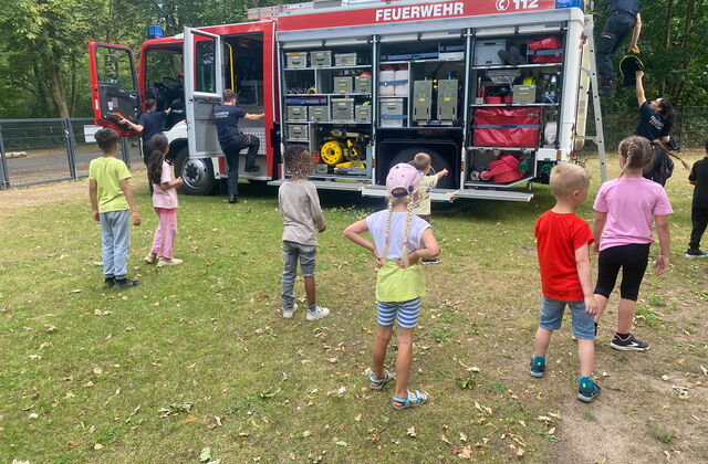 Kinder bei einem Feuerwehrauto. Feuerwehrleute zeigen Material.