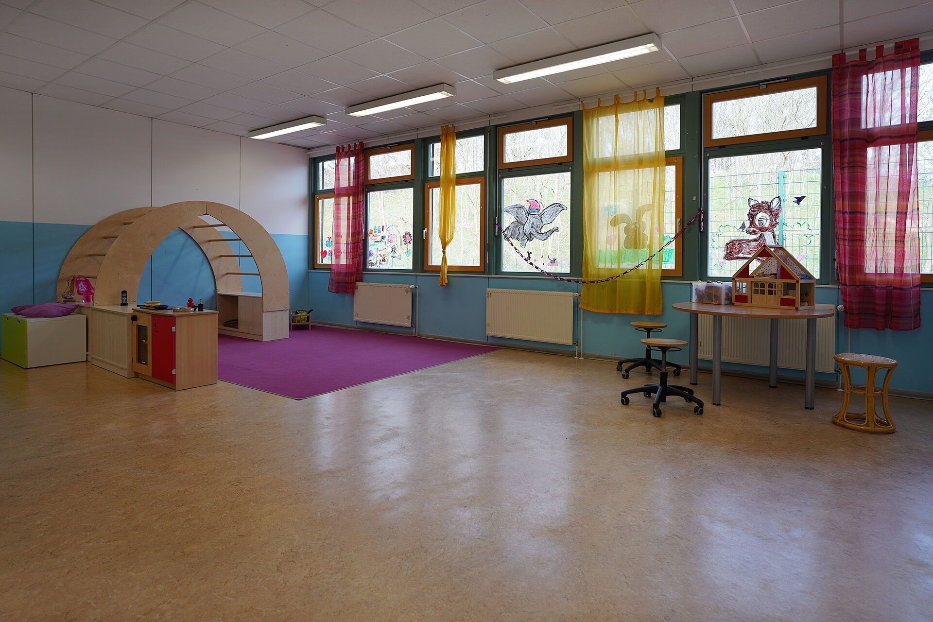 Großer Raum, mit farbigen Vorhängen vor den Fenstern, an den Fenstern Fensterbilder von Dumbo, und Bambi.
