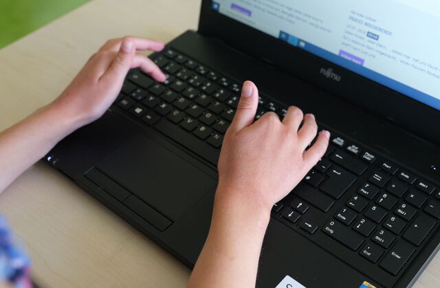 Aufgeklappter Laptop, Schüler Laptop. Kinderhände tippen auf der Tastatur des Laptop.