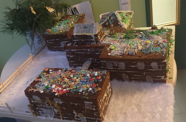 Lebkuchen-Kita-Komplex mit weißem Zeug das Schnee darstellen soll. Die Lebkuchen-Gebäude sind bunt mit Süßigkeiten dekoriert. Sie steht auf einem runden Tisch.