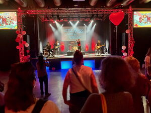 Auf der Bühne eine Band davor ein paar Menschen. Luftballons sind an der Bühne befestigt.