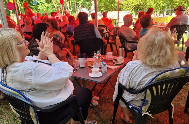 Menschen sitzen an kleinen Gartentischen bei Kaffee und Kuchen und klatschen.