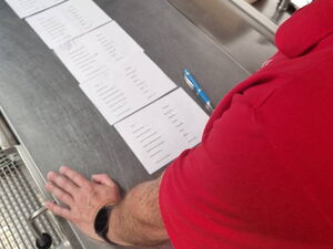 Mann in roter Kleidung steht in Großküche. Er begutachtet Listen.