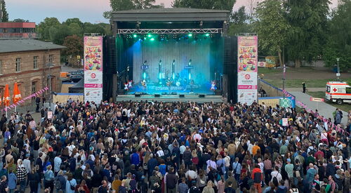 Eine große Bühne, rechts und links davon Banner vom Akzeptanzfestival. Vor der Bühne viele feiernde Menschen. Auf der Bühne eine Band.