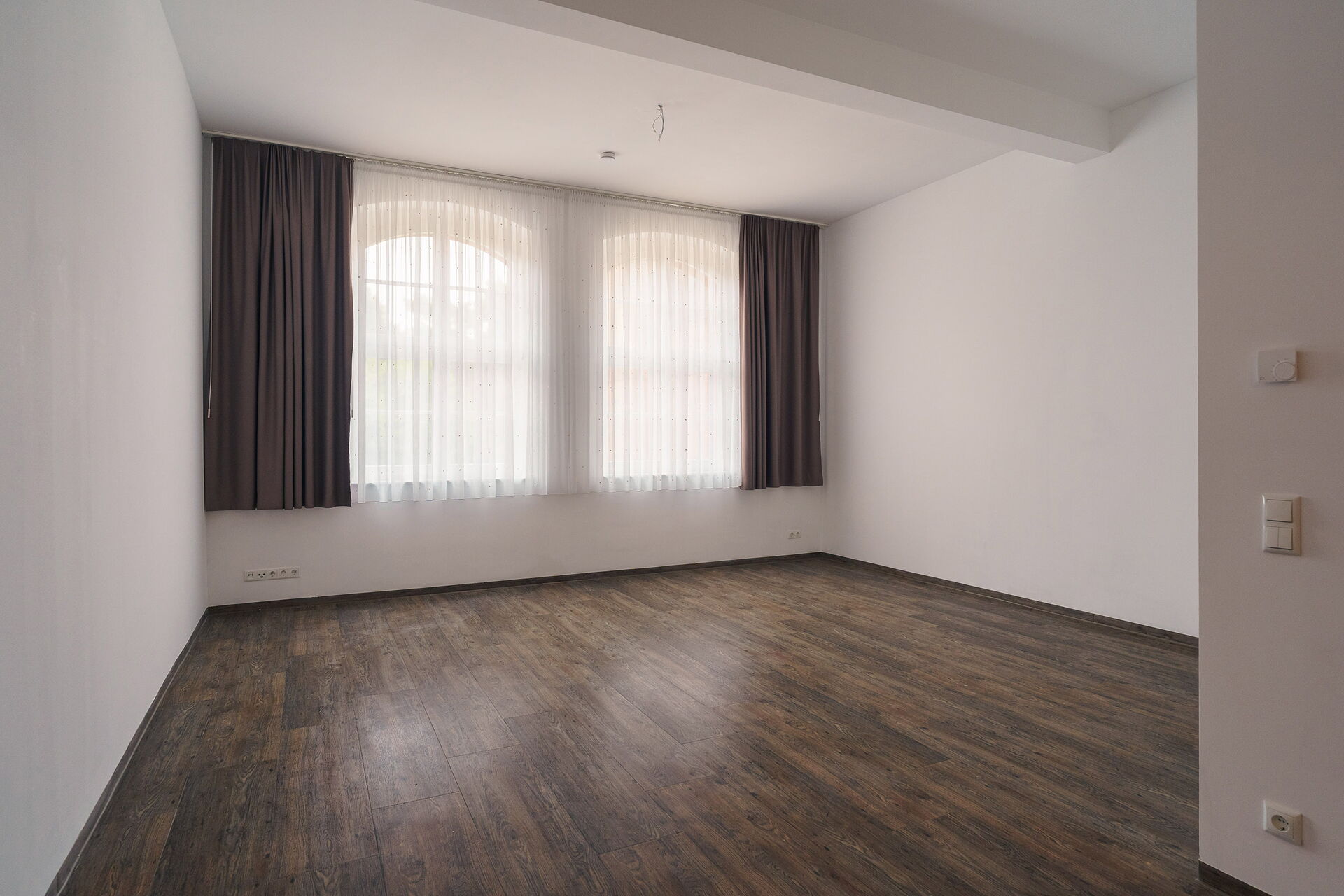 Leeres großes Zimmer / 1-Raum-Wohnung mir großen Fenstern mit Vorhängen.