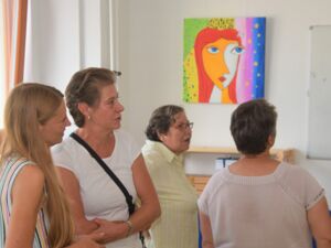 Vier Frauen in dem Ausstellungsraum. An der Wand hängt das abstrakte Bild der Frau mit dem bunten Hintergrund. Die Besucherinnen schauen sich um.