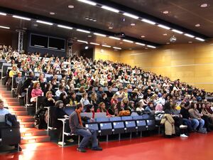 Hörsaal einer Uni. Gut besucht, fasst alle Plätze sind besetzt.