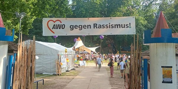Eingang zum Festival mit Banner über dem Zugang. Text: AWO gegen Rassismus. Dahinter großes Festgelände mit Menschen.