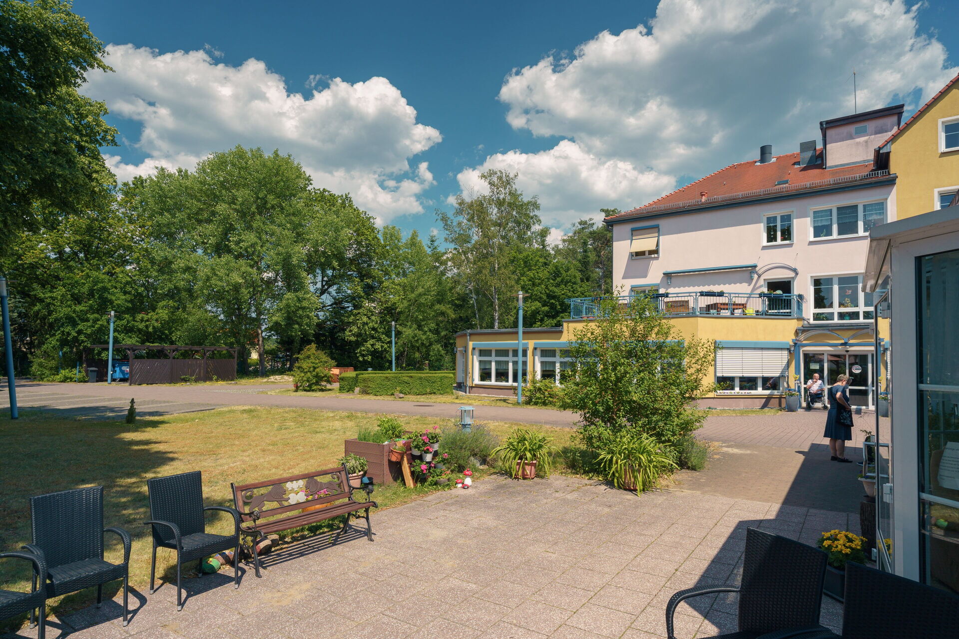 Außenbereich. Wiese, Pflanzen. Weiter hinten Bäume. Haus rechts im Bild.