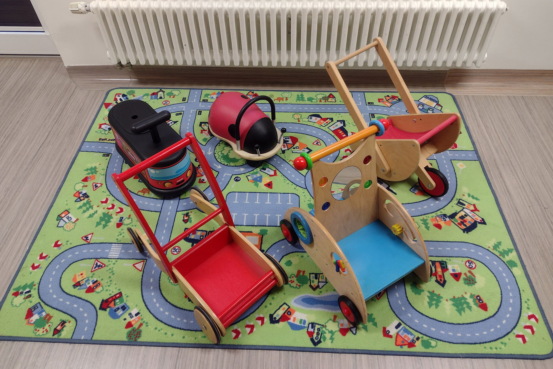 Fünf Kleinkindfahrzeuge auf einem Teppich auf dem ein Straßennetz abgebildet ist.