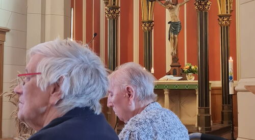 2 alte Menschen im Rollstuhl in einer Kirche.