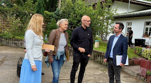 2 Frauen und 2 Männer draußen. Rechts im Hintergrund ein weißes Haus.