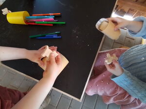 Zwei Kinder an einem Tisch. Auf dem Tisch liegen Stifte. Ein Kind hält eine kleine Holz-Tier-Katze in der der Hand. Das andere Kind ein Holz-Tier-Pferd.