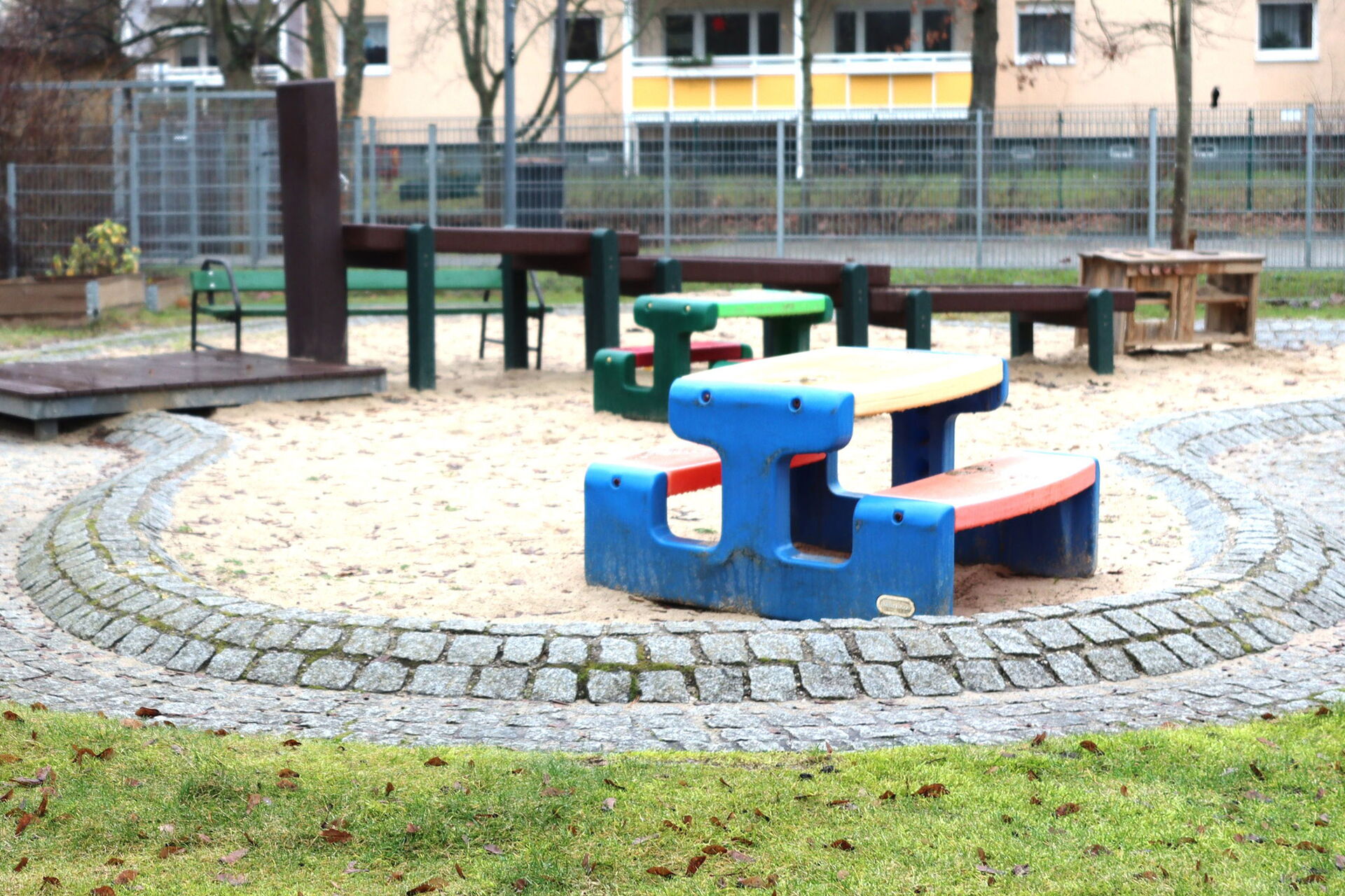 Spielgeräte vor einer Kita. Farbige Sitzgelegenheiten, Sandkasten, Wasserspielplatz.