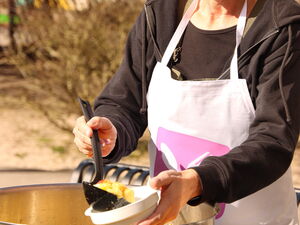 Draußen, Sonne scheint. Großküchen Topf eine Frau mit Schürze mit eine Keller befüllt eine Schale mit Essen.