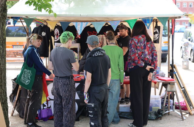 Stand mit T-Shirts, Beuteln und mehr. Davor interessierte Jugendliche und junge Erwachsene.