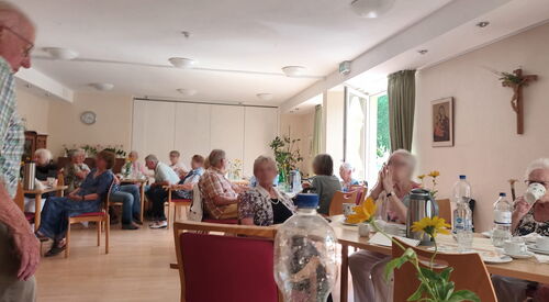 Raum, mehreren Tischen an denen Menschen sitzen. Kaffee und Wasserflaschen auf den Tischen.
